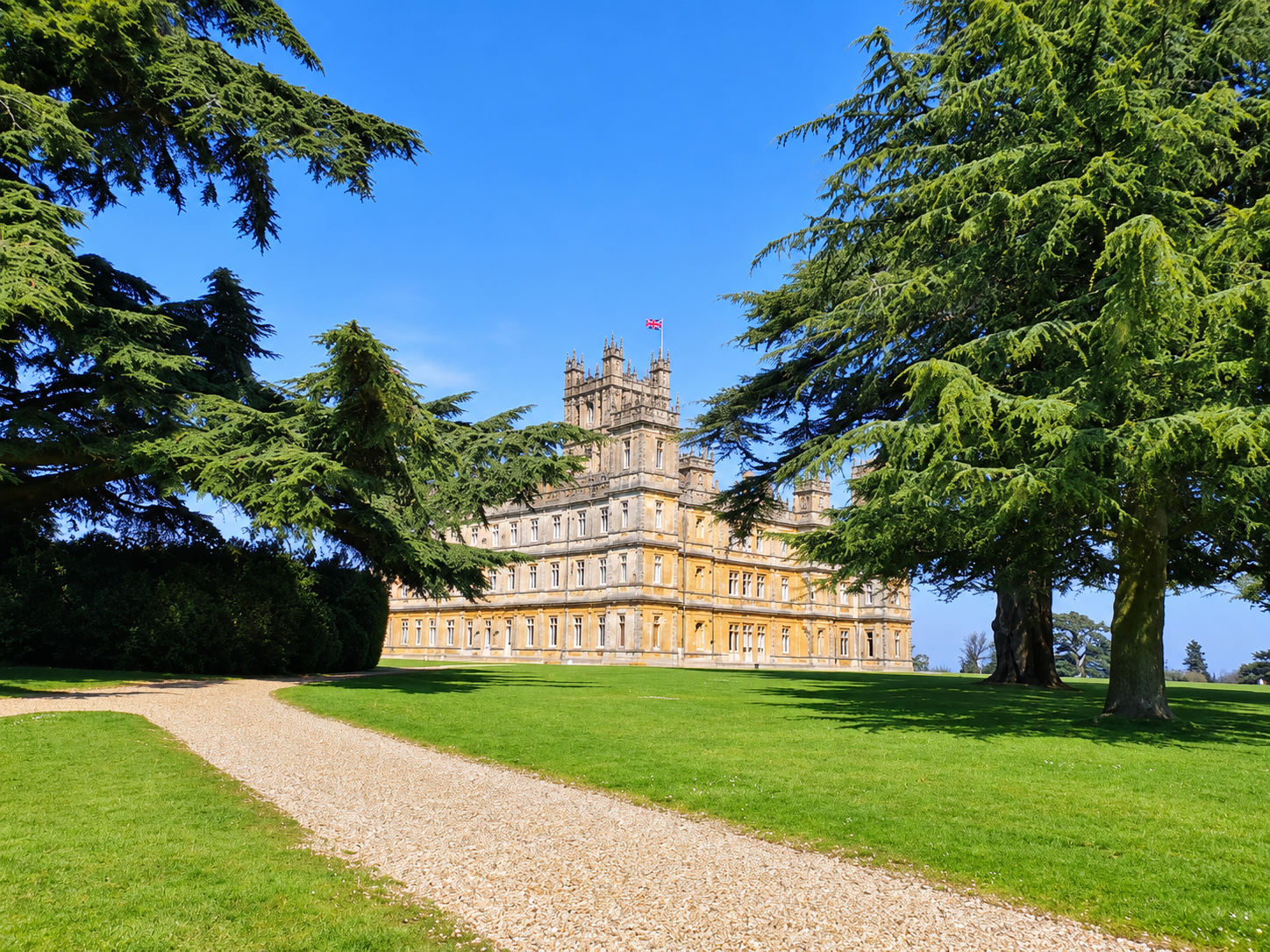 Grand English country house inspired by Highclere Castle, framed by mature trees and lawns on a bright summer day