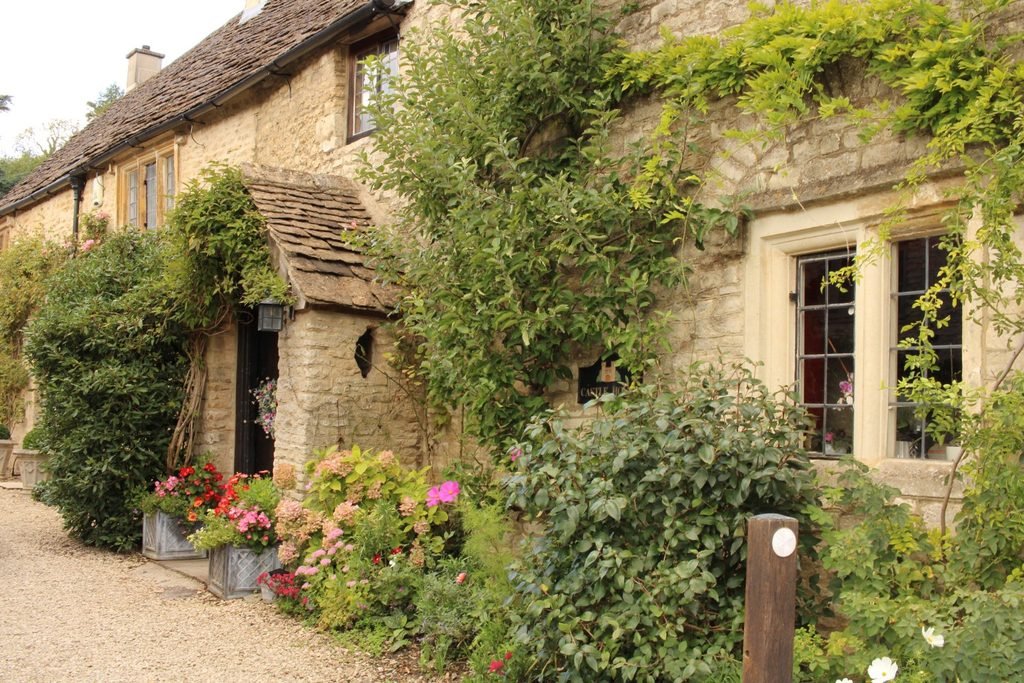 Old stone cottage in Castle Combe covered with climbing greenery and colorful flowers around the windows and doorway