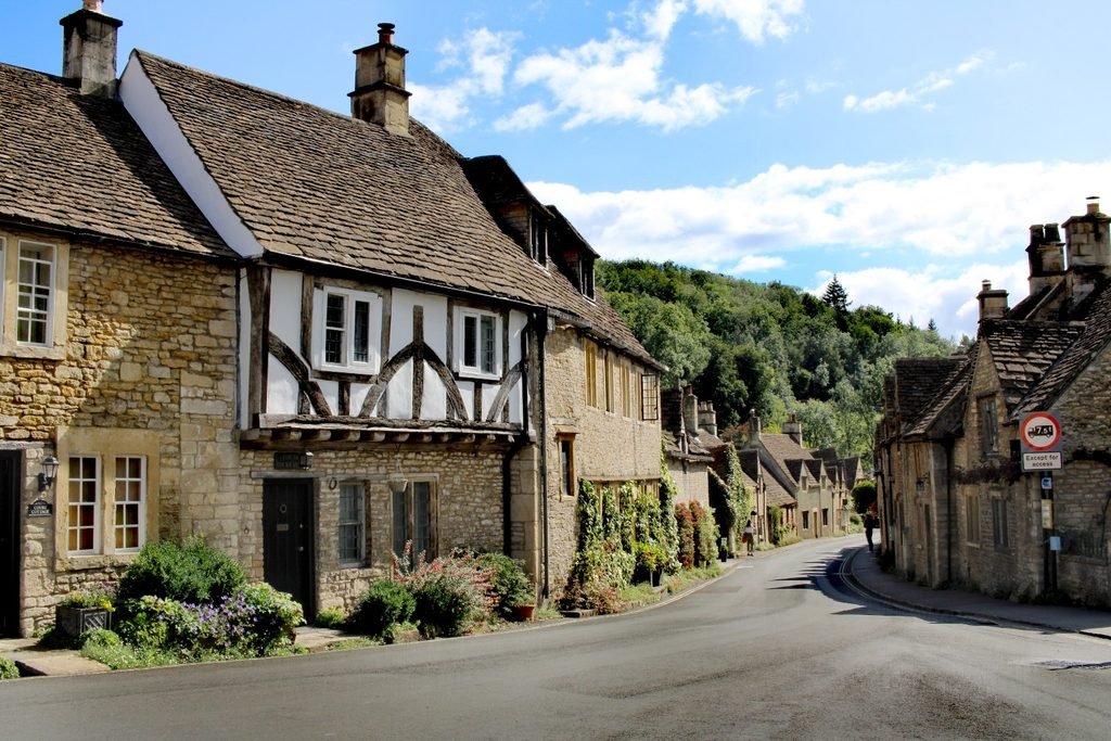Quiet street in Castle Combe lined with historic stone cottages under a bright blue sky