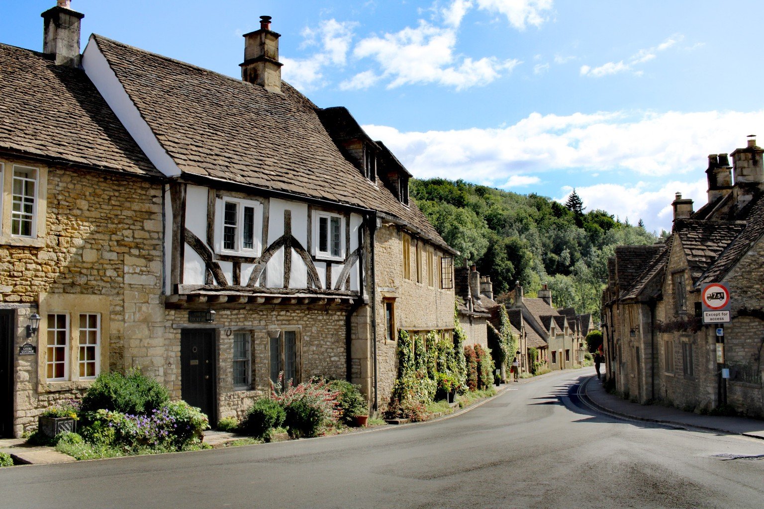 Quiet street in Castle Combe lined with historic stone cottages under a bright blue sky