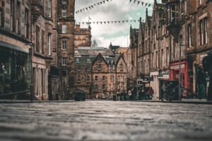 Stone buildings, colorful bunting, and pedestrians along a cobbled Edinburgh street beneath a cloudy sky